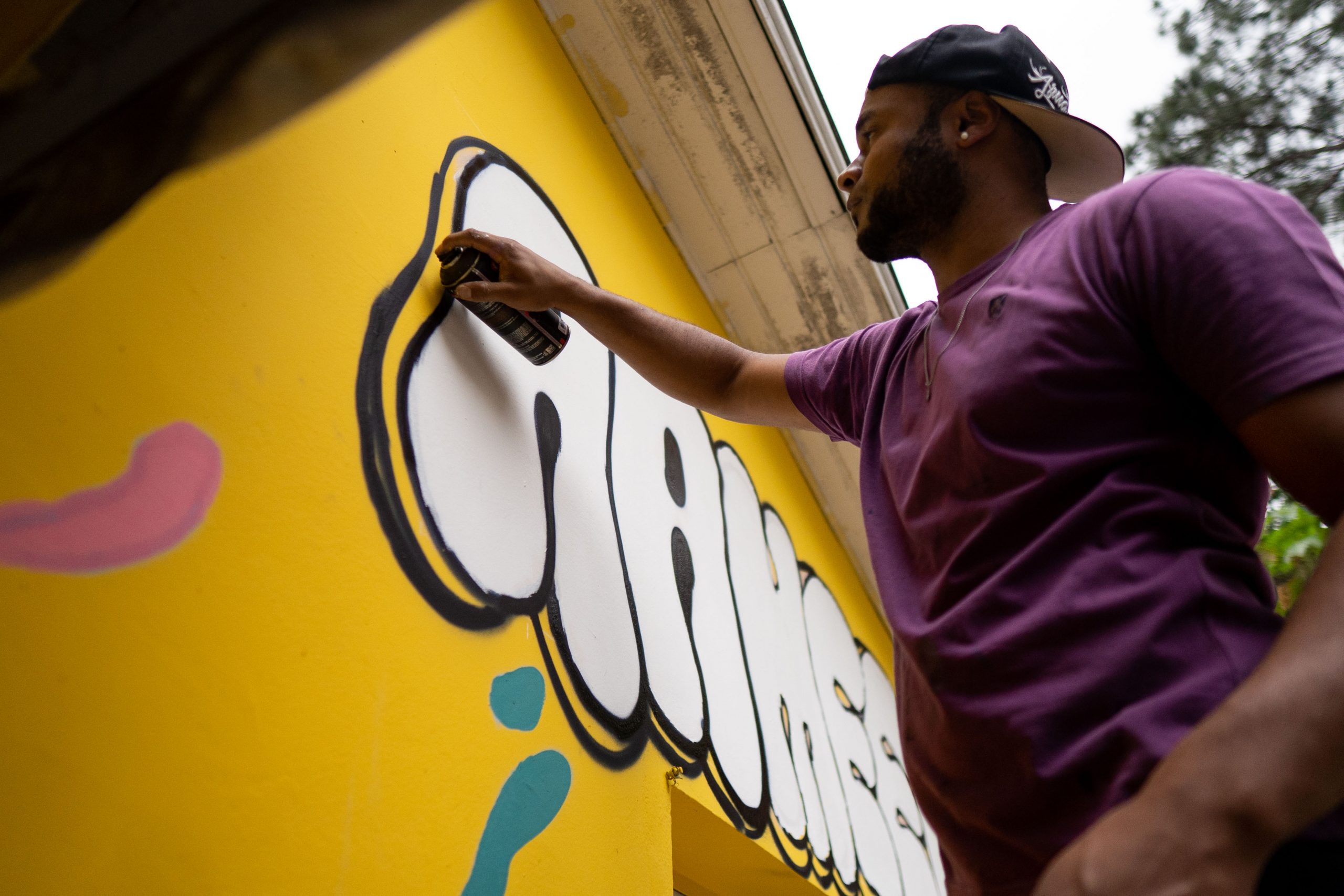 Fotografia de um homem segurando uma lata de tinta e desenhando um grafite na parede.