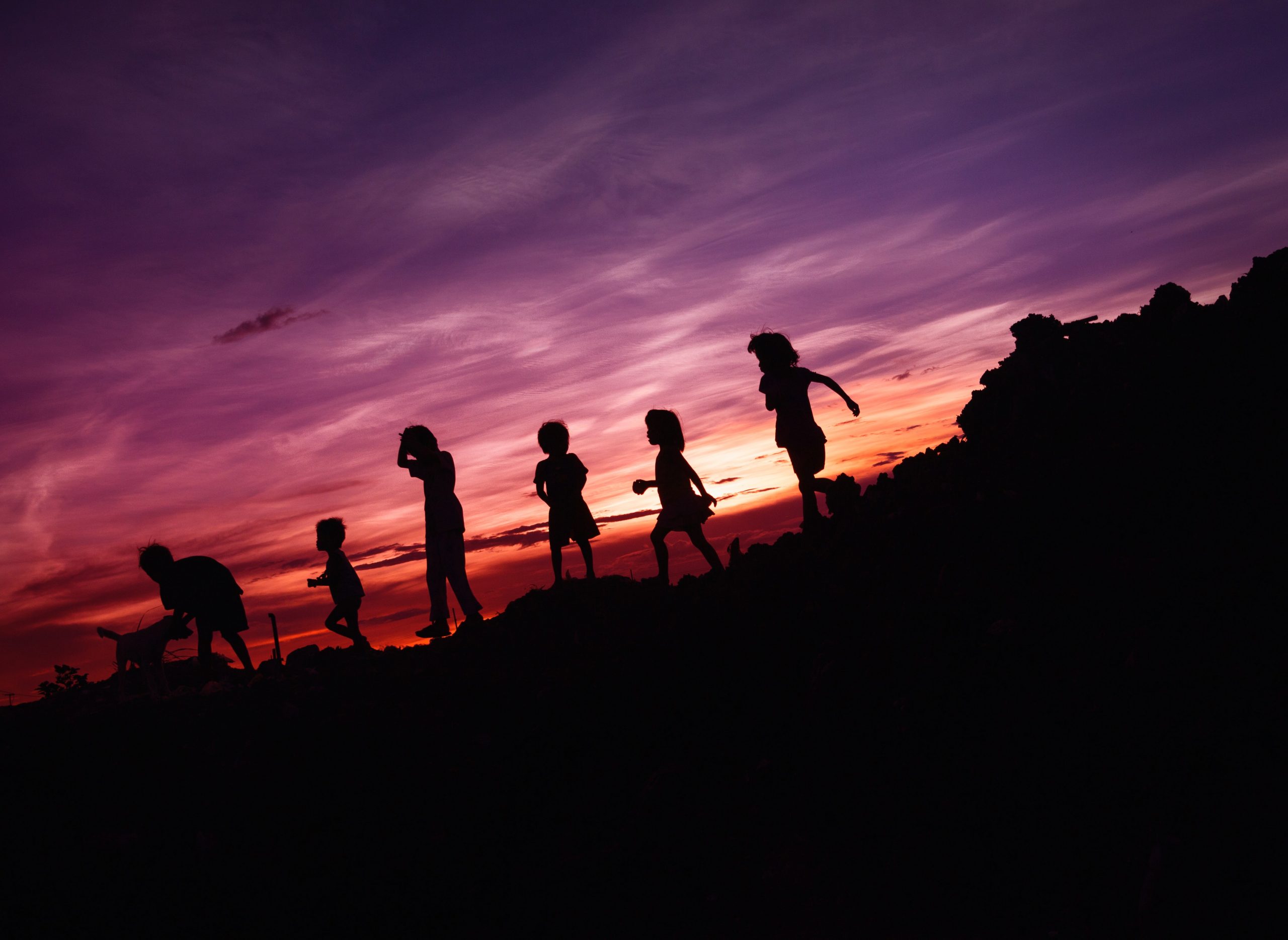 Fotografia de um pôr-do-sol. Nela, é possível ver a silhueta de seis crianças descendo uma colina.