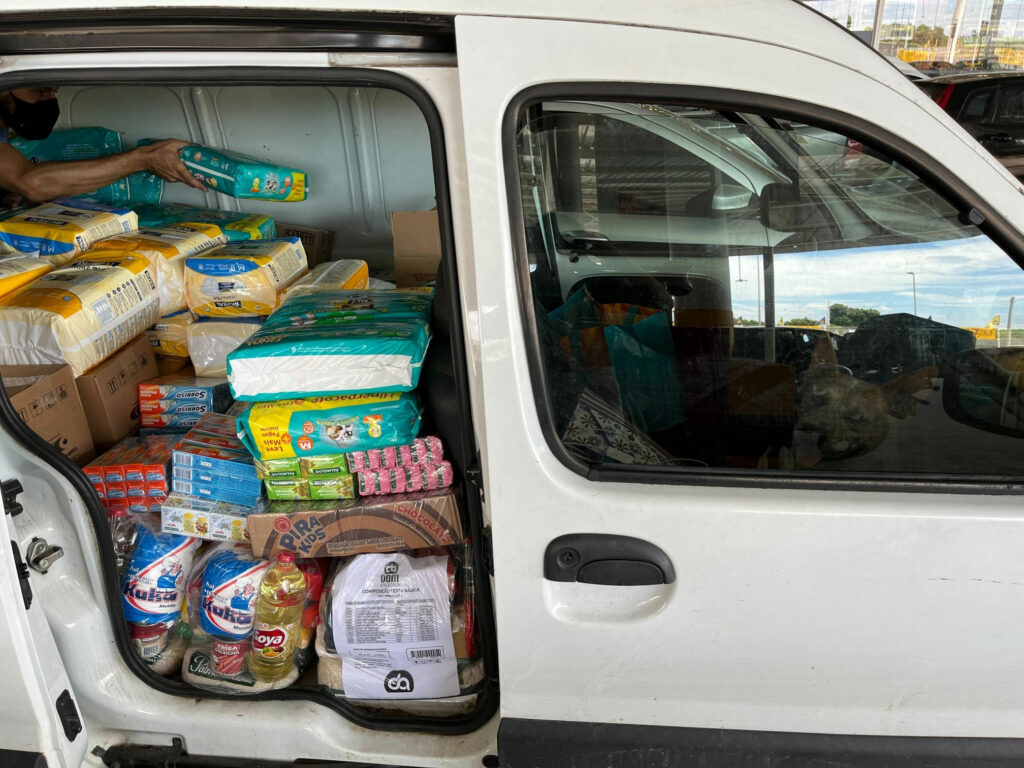 Fotografia do interior de uma van branca com diversos itens comprados com as doações, como pacotes de fraldas e cestas básicas.