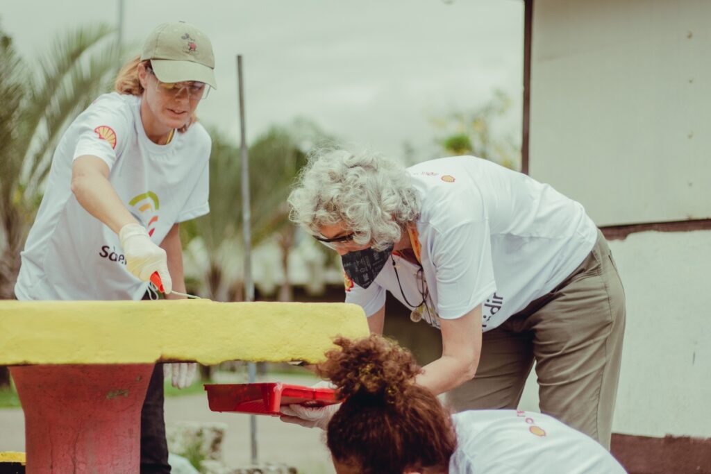 Fotografia e dois voluntários em uma ação mão na massa de voluntariado. Os dois pintam uma estrutura.